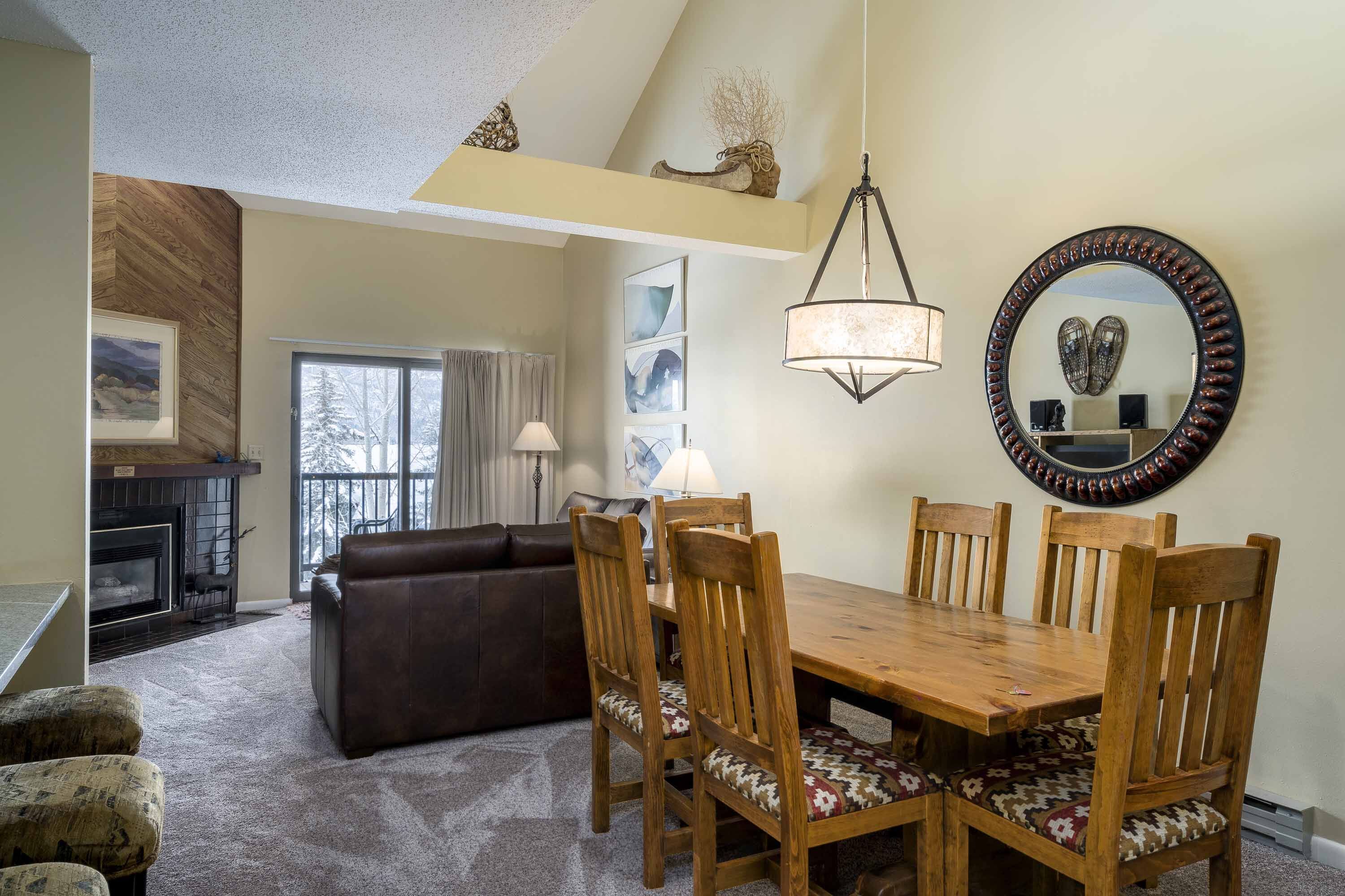 A dining area with a wooden table and chairs, a fireplace, a sofa, and a large mirror on the wall.