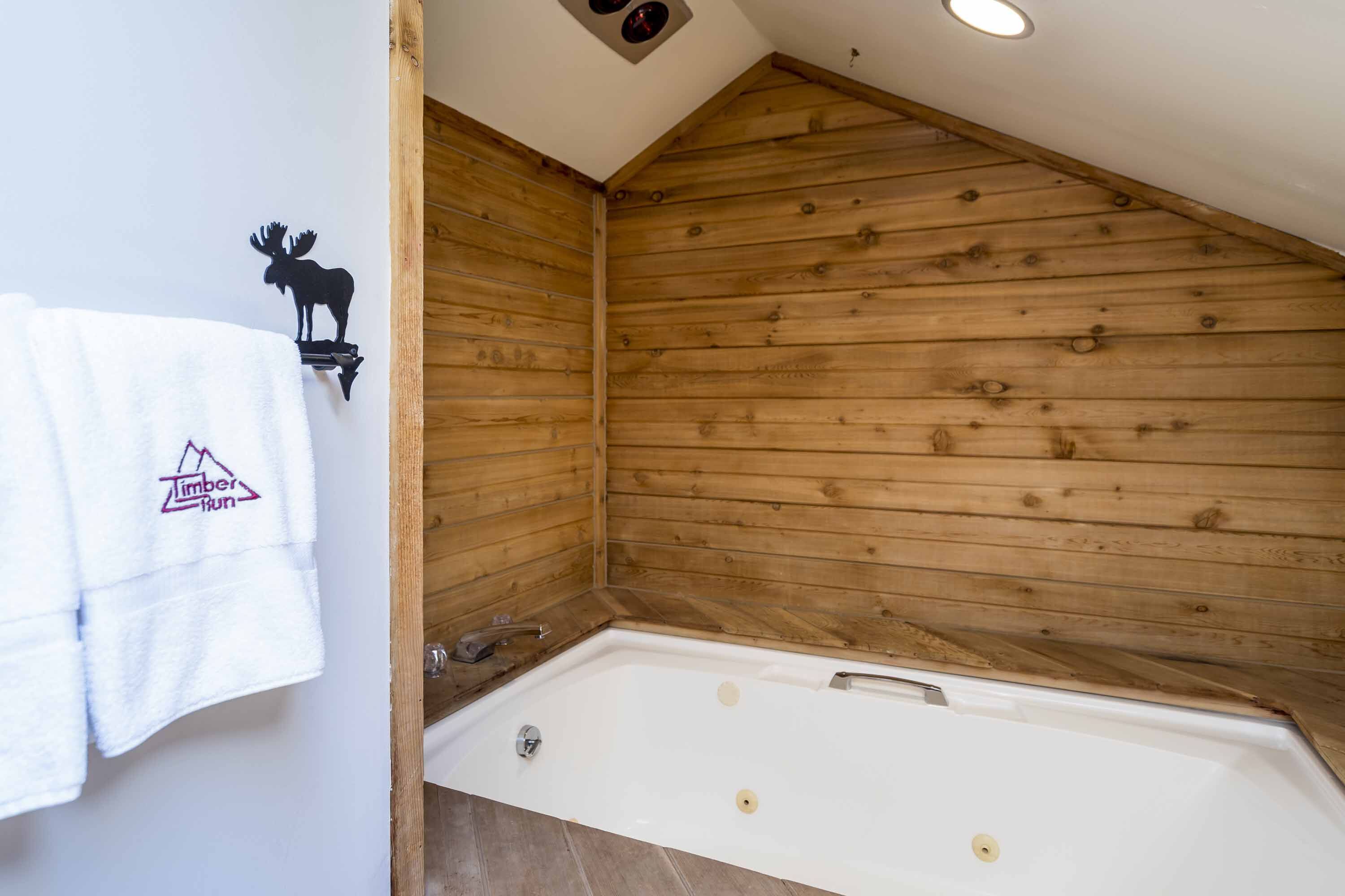 Un baño estilo cabaña de madera con una bañera, una toalla con un logotipo y una decoración de alce.