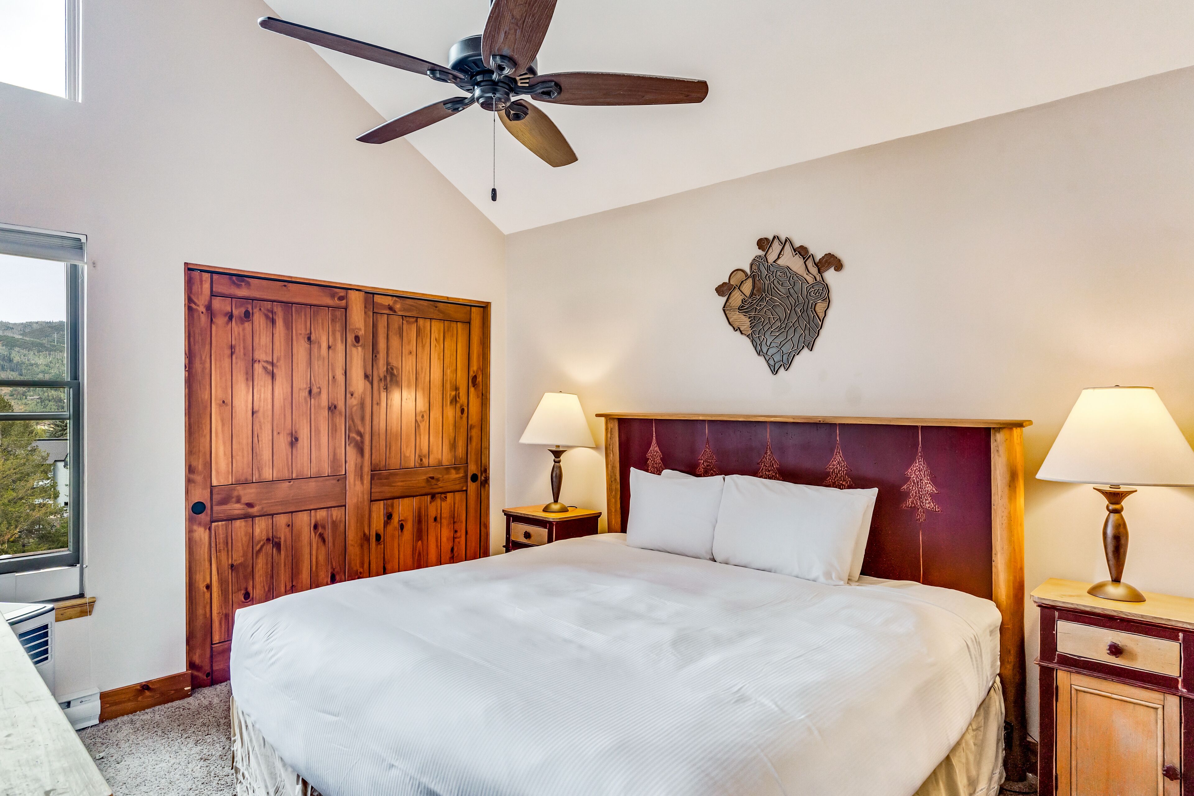 Ein Hotelzimmer mit einem großen Bett, einem Holzschrank, einem Deckenventilator, einer Wanddekoration und zwei Nachttischlampen.