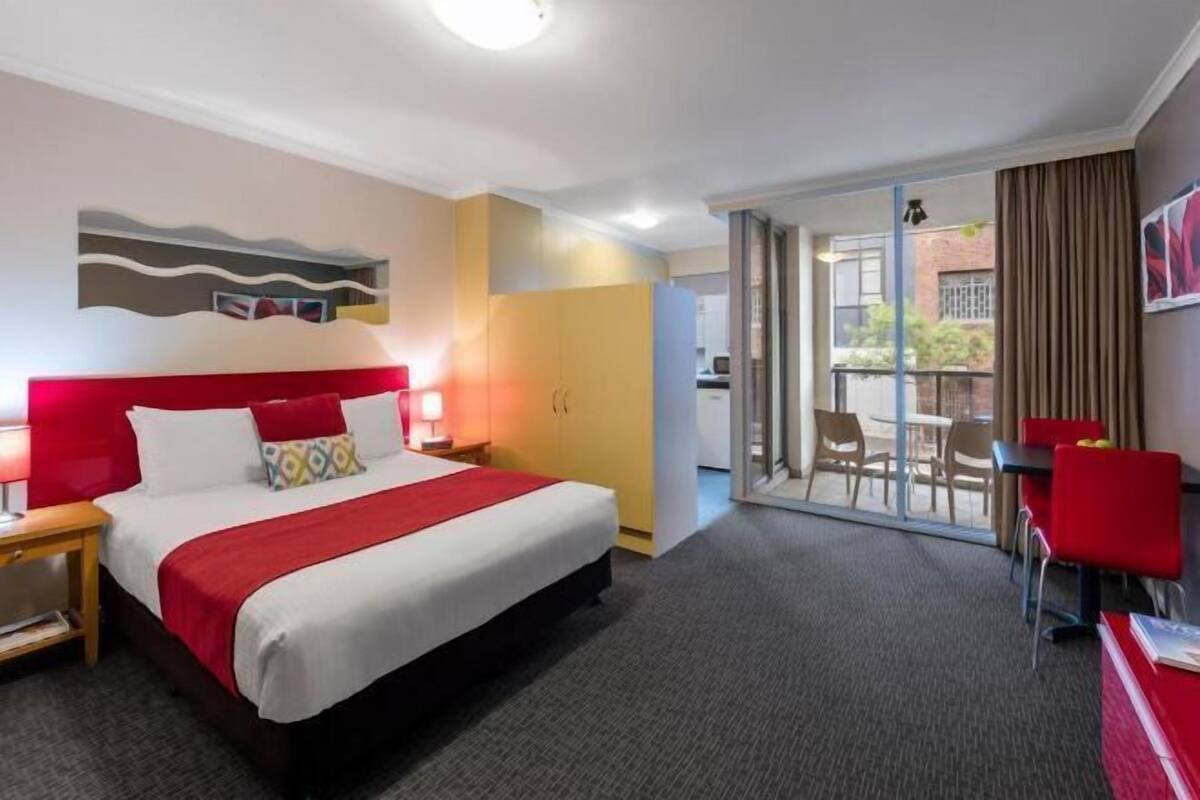 A hotel room with a bed, a desk, a chair, and a view through a glass door.