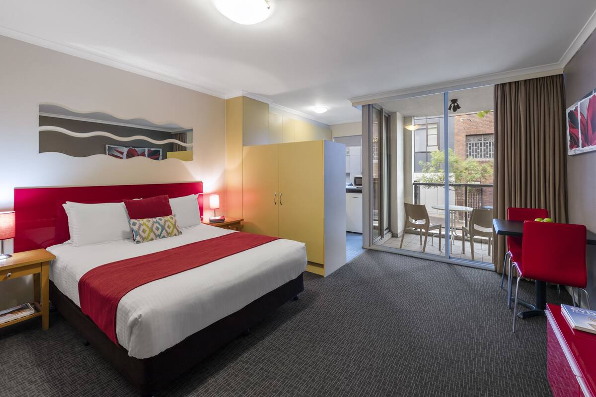 A hotel room with a bed, a desk, a chair, and a balcony with a table and chairs.