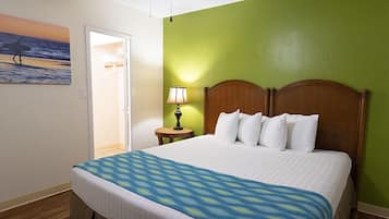 A hotel room with a bed, a nightstand with a lamp, a painting of a beach scene, and a ceiling fan.