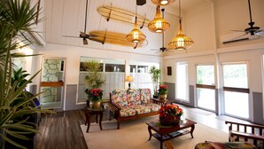 A spacious living area with a sofa, coffee table, and hanging lights. There are potted plants and a ceiling fan.