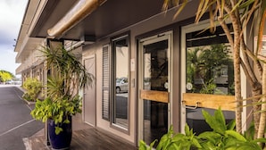 A hotel entrance with a wooden bench, potted plants, and a glass door.