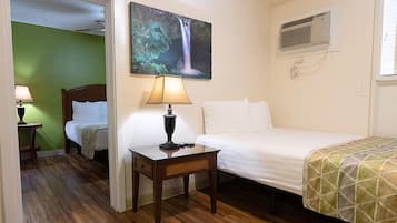 Hotelkamer met twee bedden, nachtkastje met lamp, schilderij van een waterval, airconditioning en een groene wand.