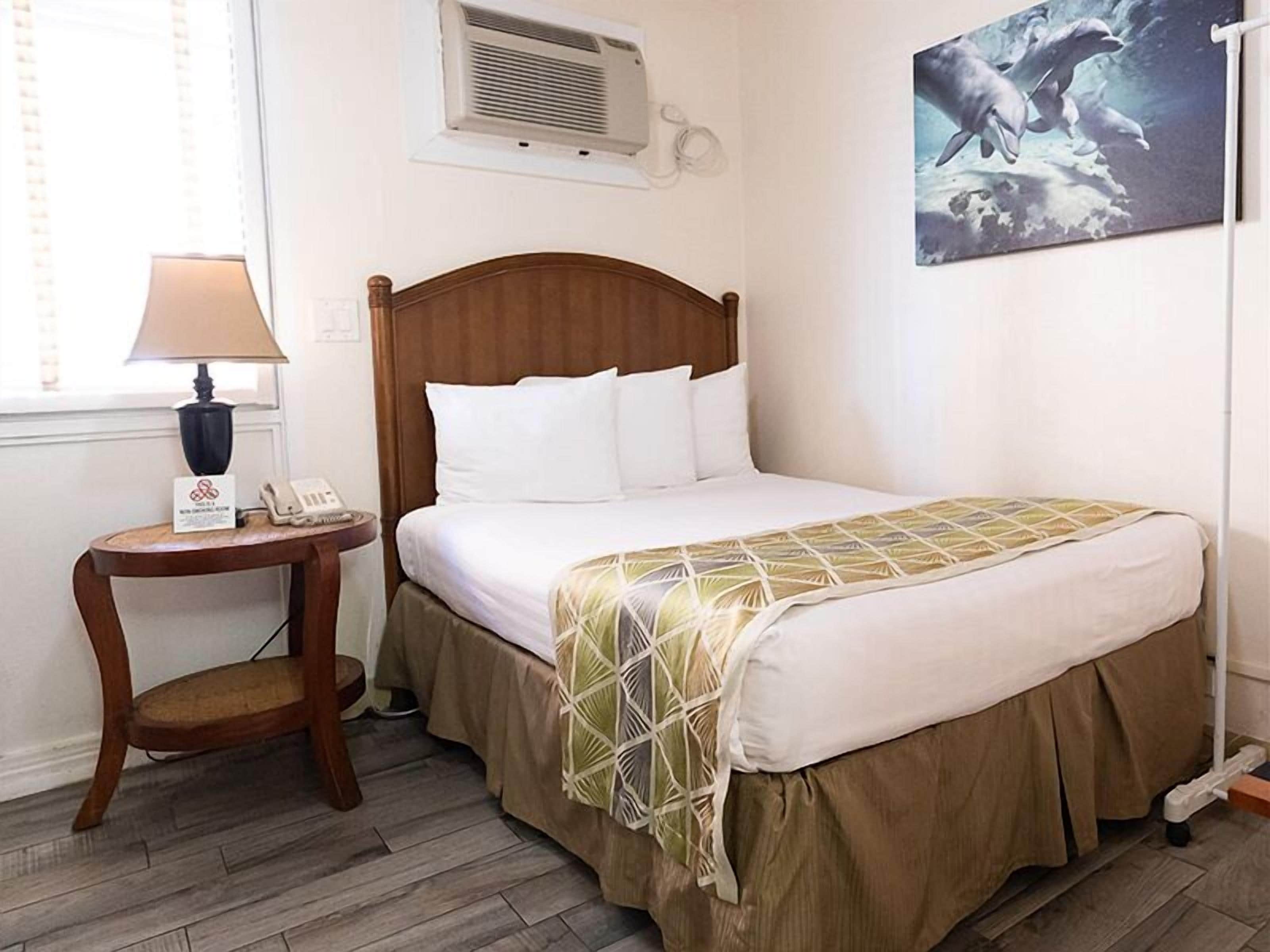 Habitación de hotel con cama de madera, una mesita de noche con lámpara, teléfono y un cuadro con delfines en la pared.