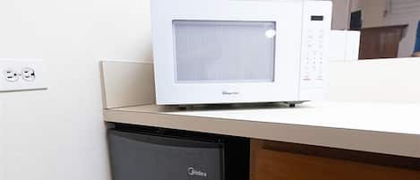 A microwave oven on a white countertop with a small black appliance below it.