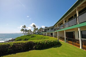 A hotel with a balcony overlooking the ocean, a grassy area, and palm trees. - Castle at Makahuena at Poipu (Koloa)