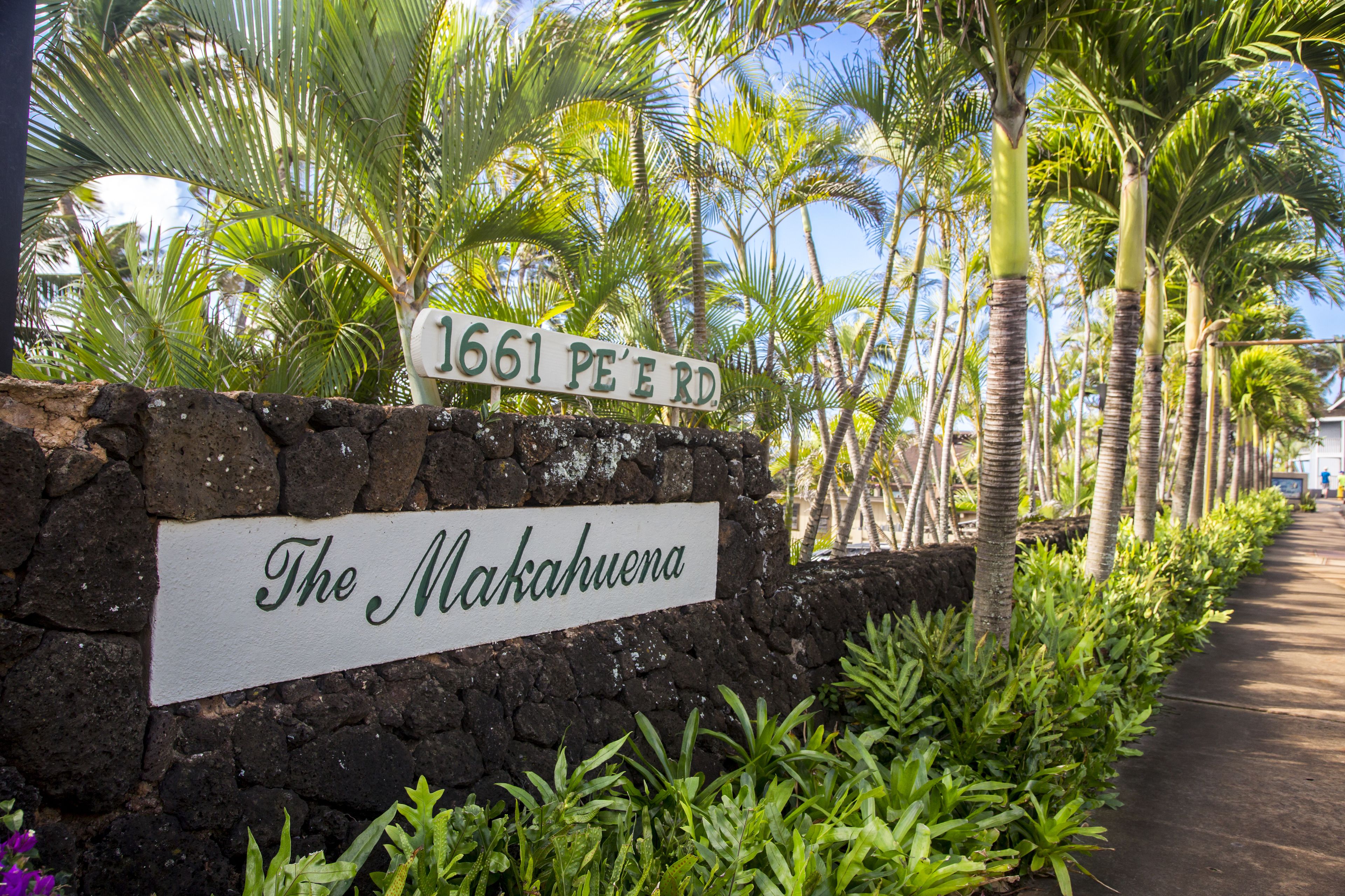 A sign with '1661 PE'ERD' and 'The Makahuena' written on it, surrounded by tropical plants and palm trees.