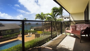 Varanda com sofá de vime, piscina e vista para o oceano e palmeiras.