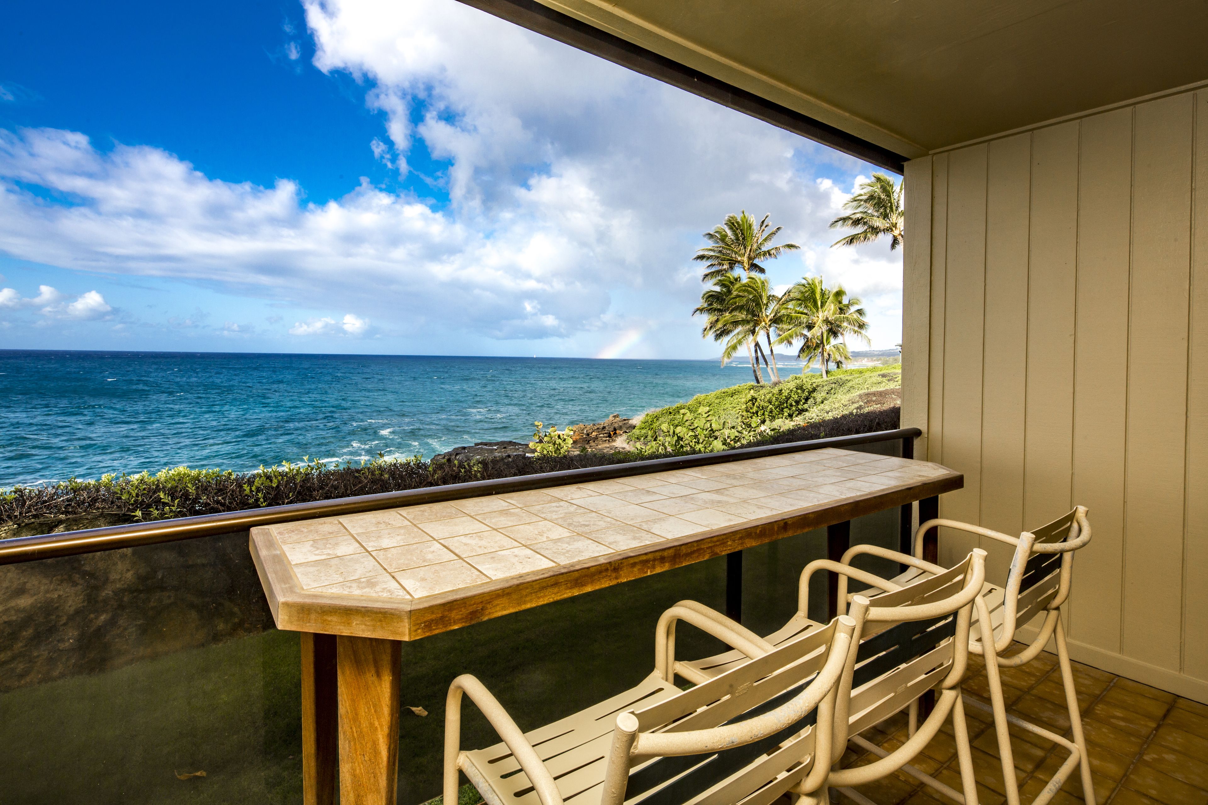 Een balkon met uitzicht op de oceaan en palmbomen.