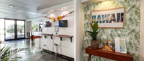A reception area with a wooden desk, two monitors, a framed picture, and a tropical wallpaper.