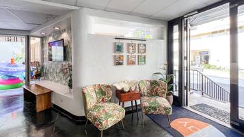 A reception area with a counter, two floral-patterned chairs, a small table, and a wall with framed pictures.