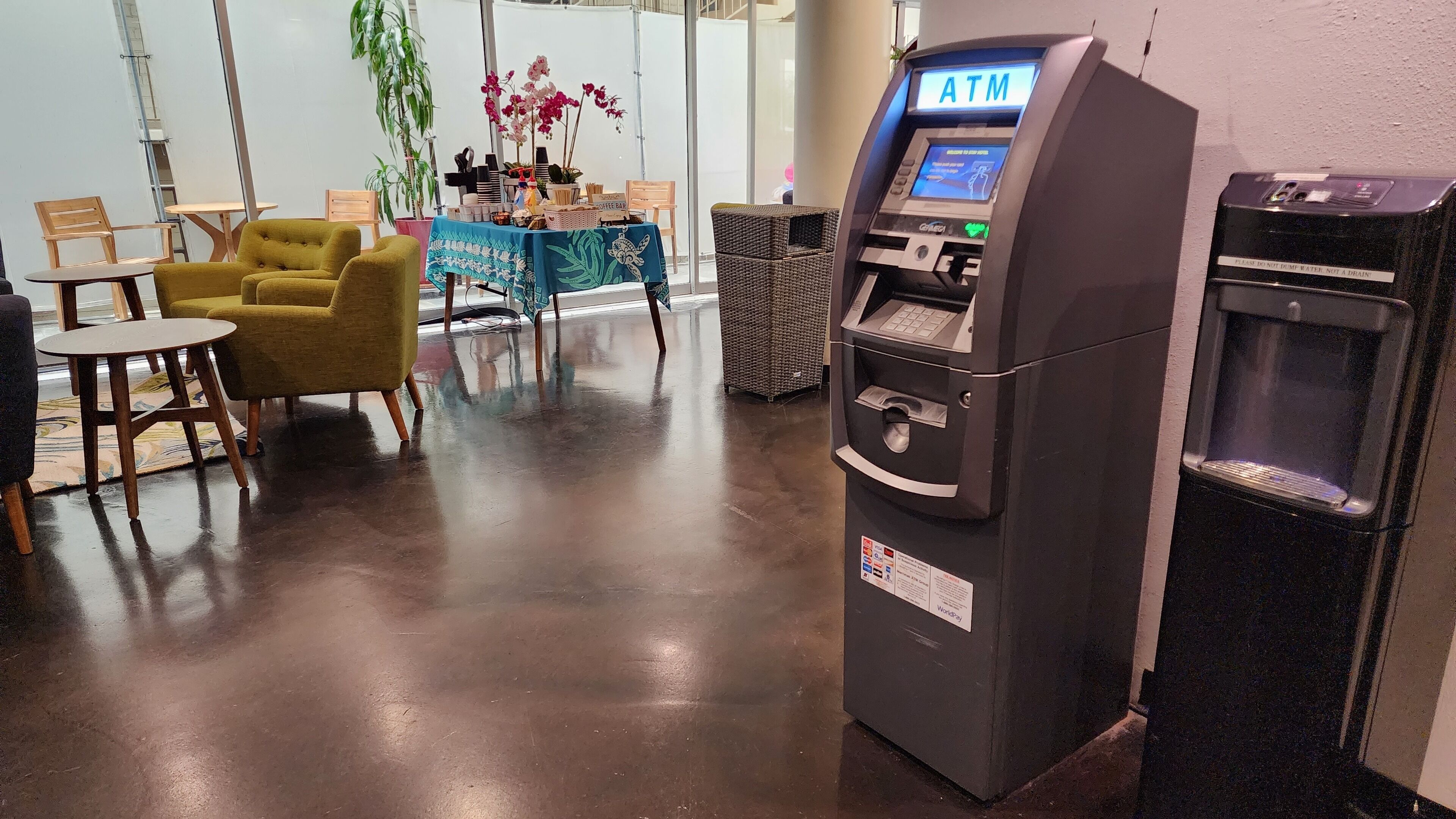 A modern indoor space with a coffee bar, seating area, and an ATM machine.