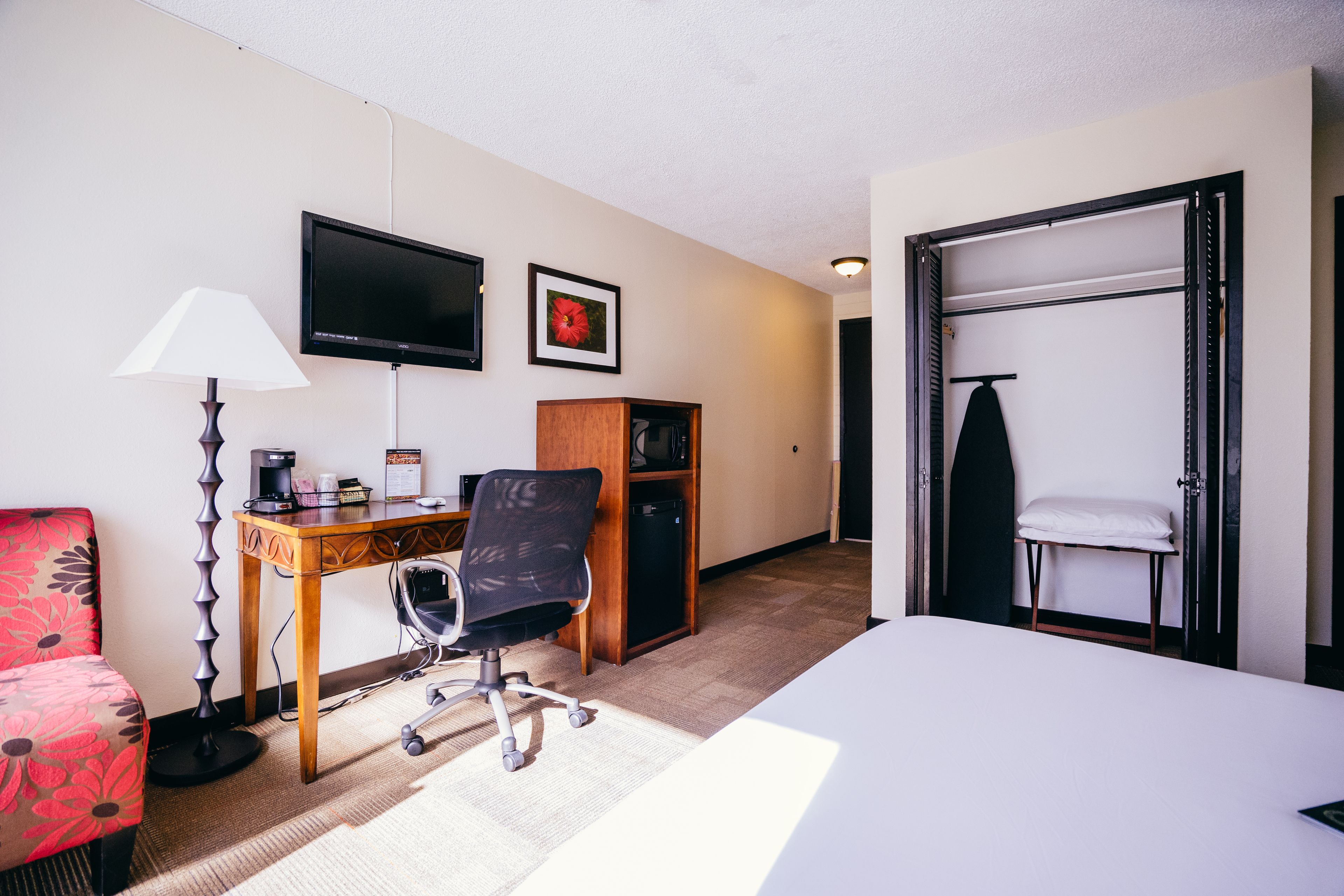 Una habitación de hotel con cama, escritorio con silla, lámpara, televisor, armario y ropero.