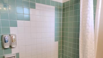 Un baño con bañera, azulejos verdes y blancos, un cabezal de ducha y una toalla blanca.