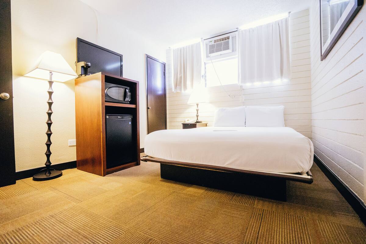 A hotel room with a bed, a desk, a lamp, and a wardrobe.