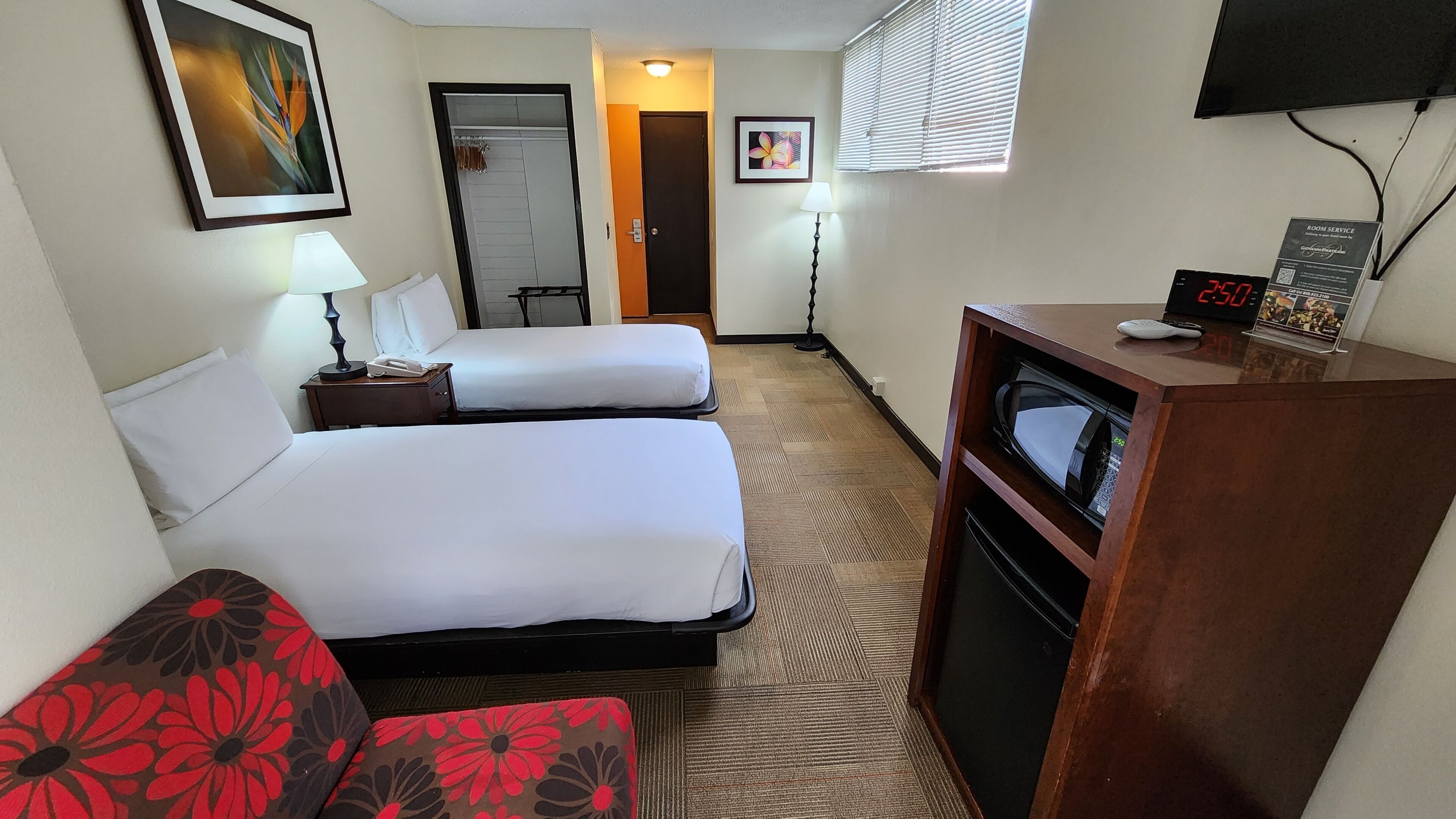 A hotel room with two beds, a desk with a microwave, a TV, and a clock displaying 2:50.