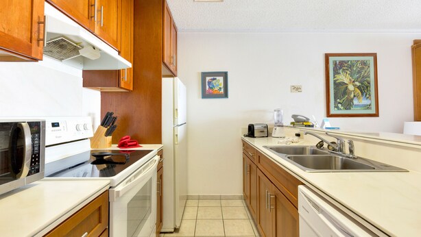 A kitchen with wooden cabinets, a microwave, stove, sink, and a toaster. - Castle at Kona Reef (Kailua-Kona)