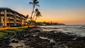 A beachfront hotel with multiple balconies overlooking the ocean, a rocky shoreline, and palm trees. - Castle at Kona Reef (Kailua-Kona)