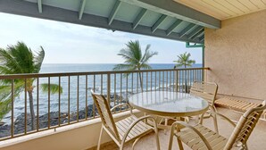 A balcony with a round glass table and chairs, overlooking a rocky coastline with palm trees. - Castle at Kona Reef (Kailua-Kona)