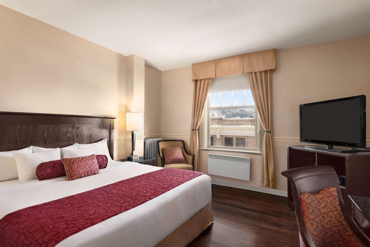 Une chambre d’hôtel avec un grand lit, une télévision, une chaise et une fenêtre avec des rideaux.