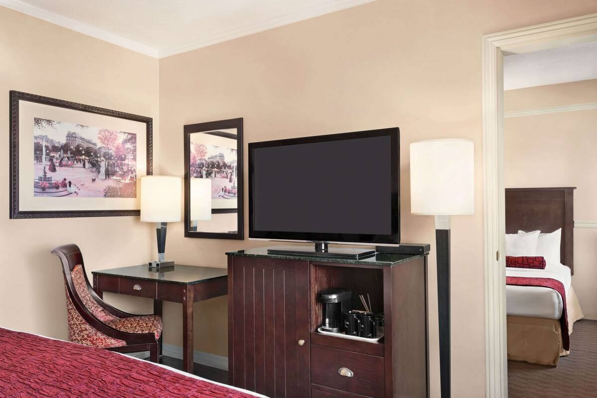 Une chambre d’hôtel équipée d’un lit, d’un bureau avec une chaise, d’une télévision, d’une machine à café et d’une lampe.