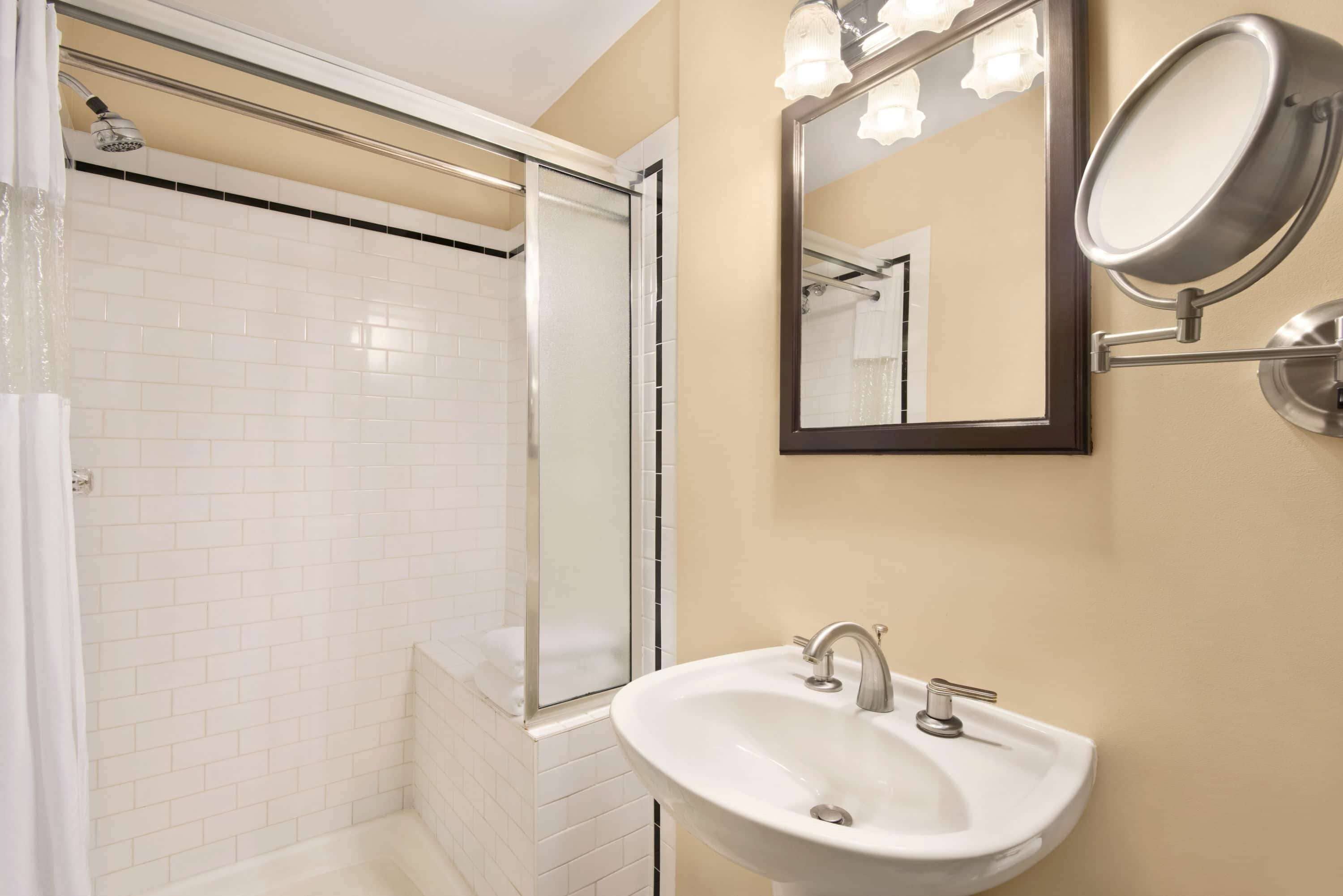 A bathroom with a glass-enclosed shower, a white sink with a mirror, and a wall-mounted light fixture.