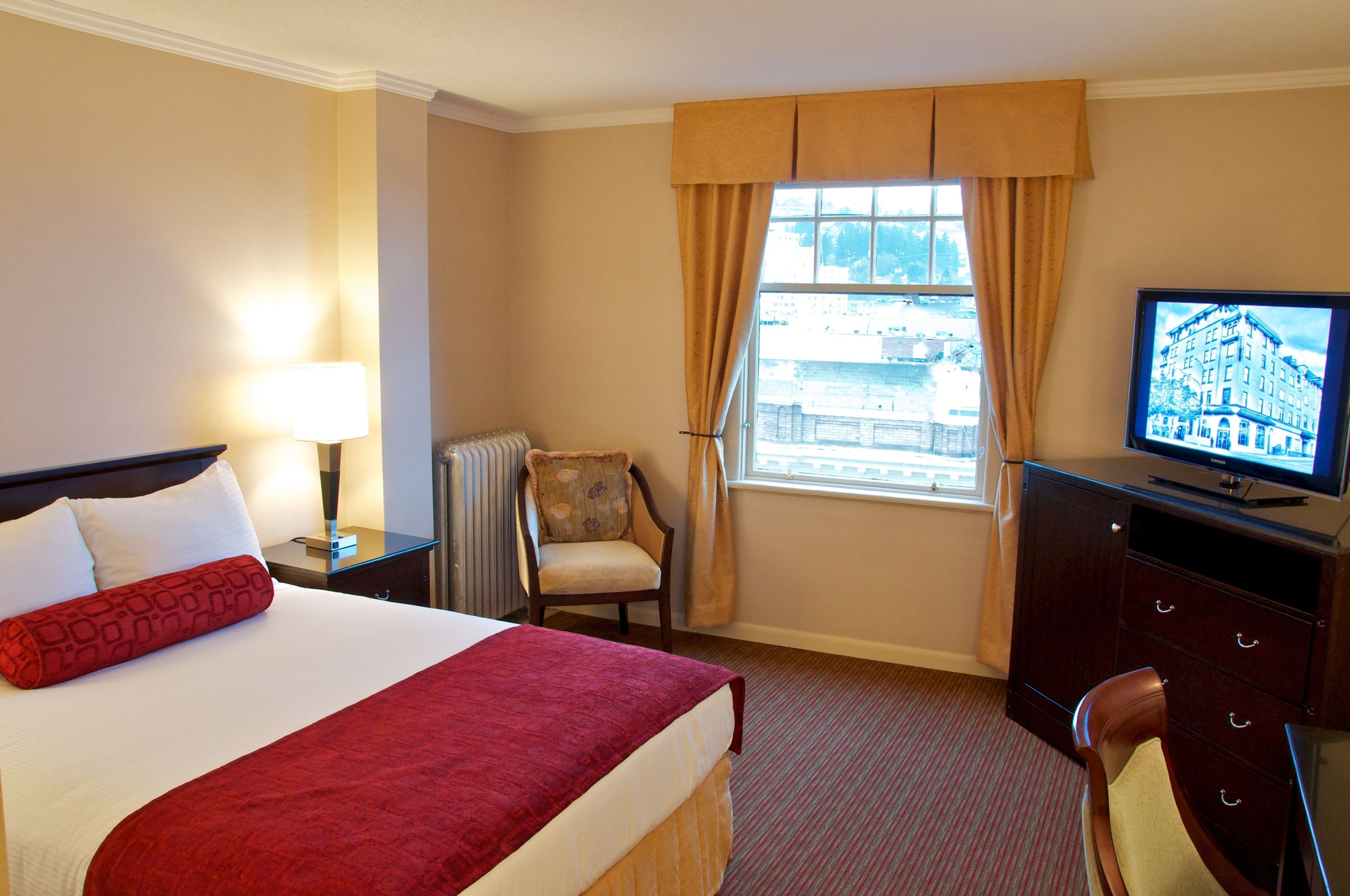A hotel room with a bed, a chair, a television, and a window with curtains.