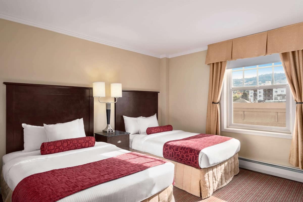Une chambre d’hôtel avec deux lits, une table de chevet avec des lampes et une grande fenêtre avec des rideaux.