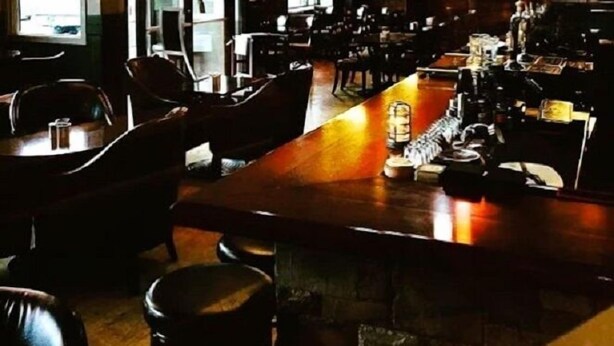A restaurant interior with a long bar, multiple tables, and hanging pendant lights. - The Plaza Hotel Downtown, Trademark Collection by Wyndham (Kamloops)