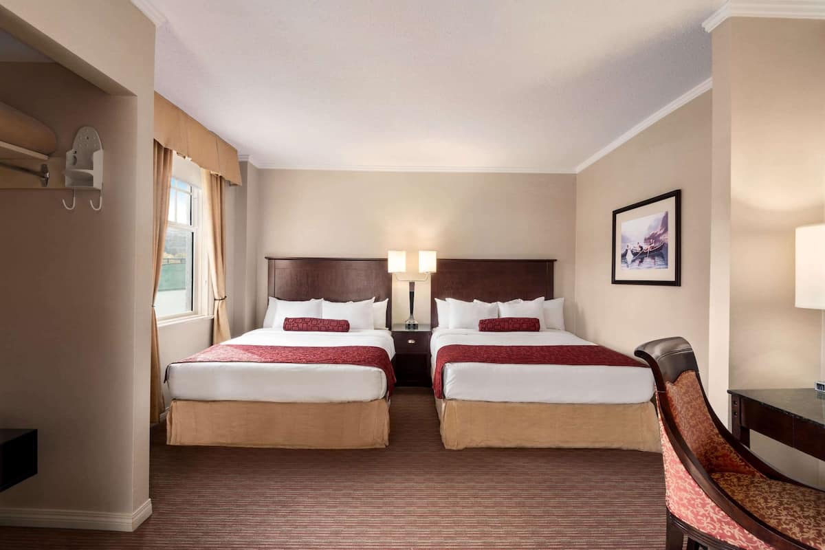 Une chambre d’hôtel avec deux lits, une chaise, un bureau, une lampe et un tableau au mur.