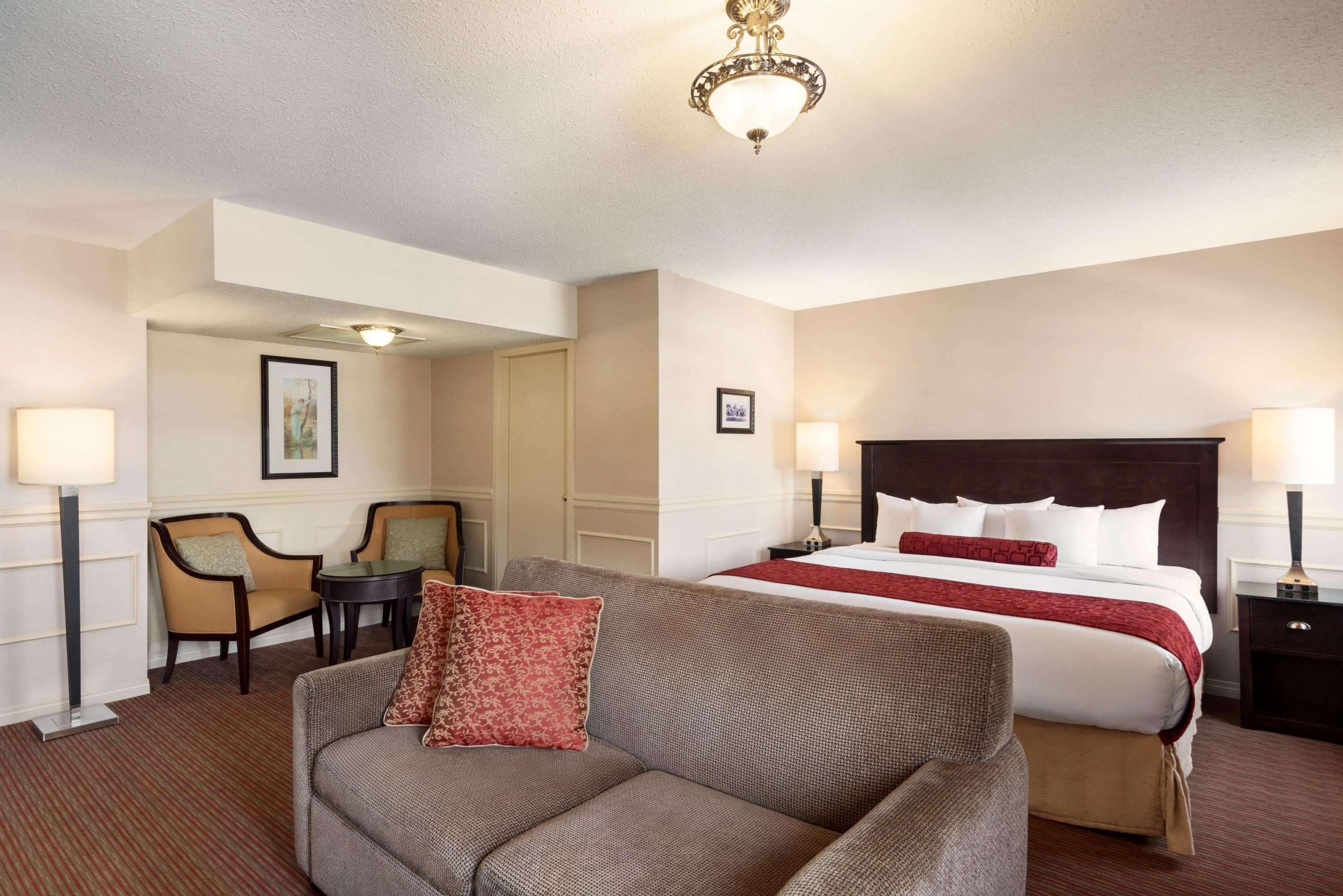 Una habitación de hotel con una cama grande, un sofá, dos sillones, una mesita y una araña.