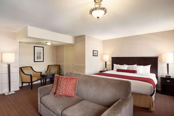 Une chambre d’hôtel avec un grand lit, un canapé, deux fauteuils, une petite table et un lustre.