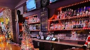 A bar area with a Christmas tree, shelves of liquor bottles, and a television screen. - The Plaza Hotel Downtown, Trademark Collection by Wyndham (Kamloops)