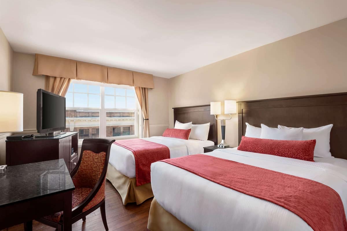 Une chambre d’hôtel avec deux lits, un bureau, une télévision et une fenêtre donnant sur des immeubles.
