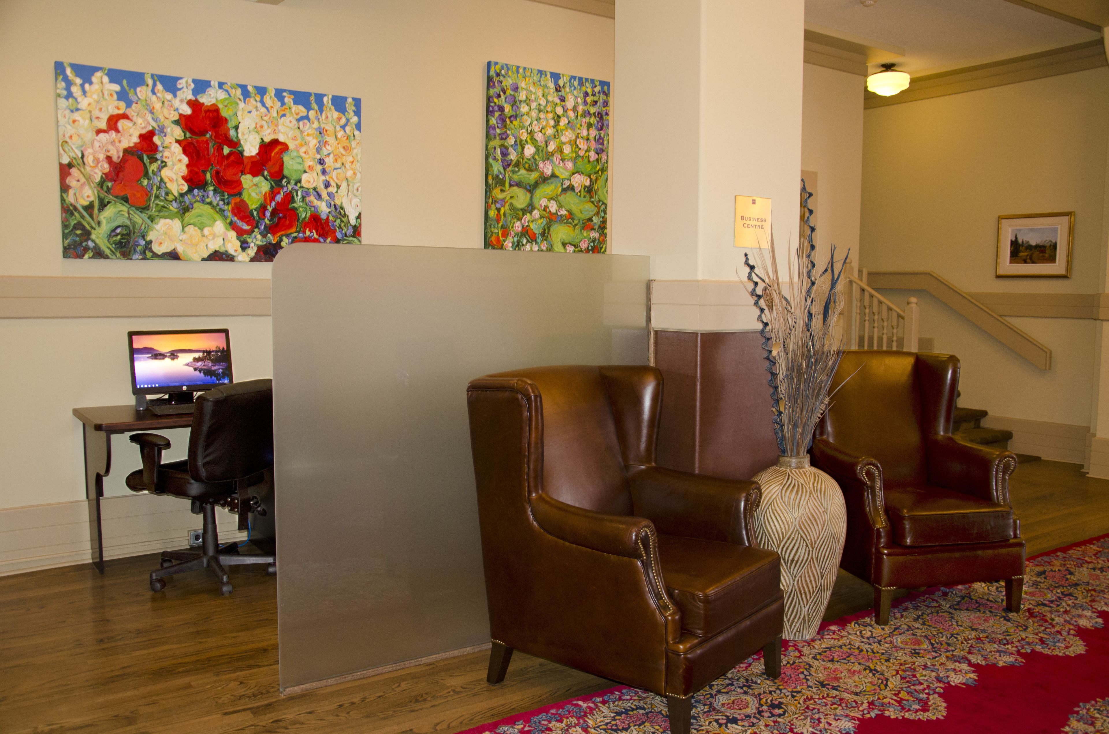A lobby with two leather armchairs, a desk with a computer, and two paintings on the wall.