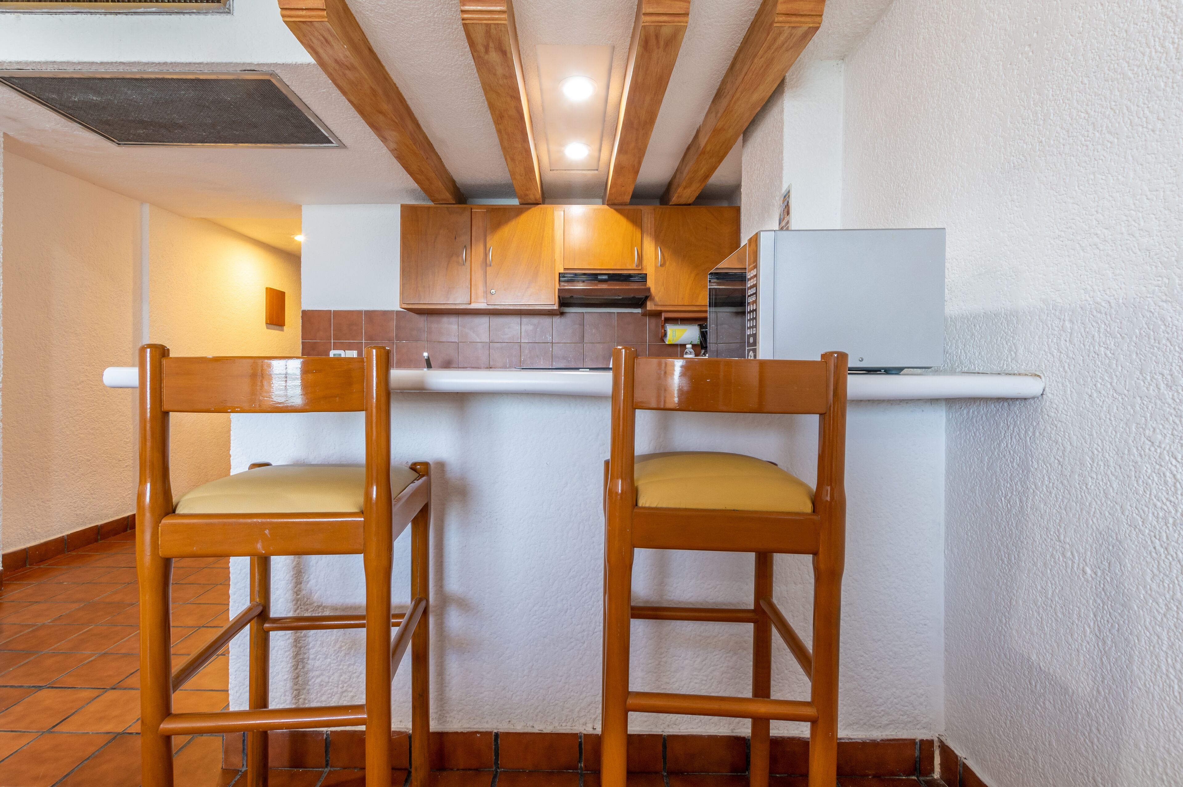A kitchen with wooden cabinets, a white countertop, and two wooden chairs with yellow cushions.