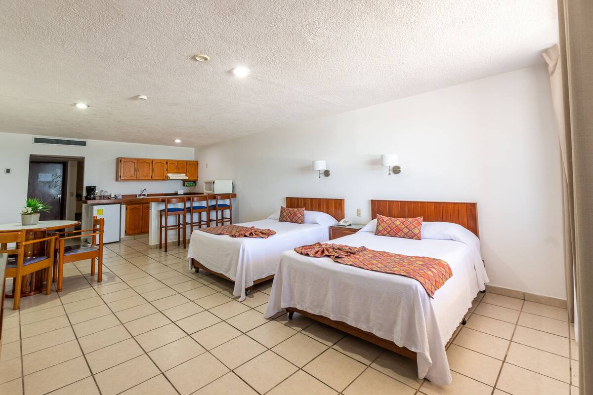 Een hotelkamer met twee bedden, een keukenhoek en een eettafel.