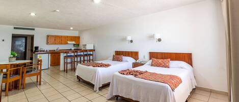 A hotel room with two beds, a kitchen area, and a dining table.