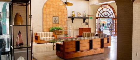 Un vestíbulo amplio con un sofá de madera en el centro, una vitrina de vidrio con objetos decorativos y un suelo de baldosas.
