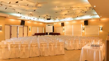 A conference room with rows of chairs covered in white, a table with water bottles, and a ceiling fan.