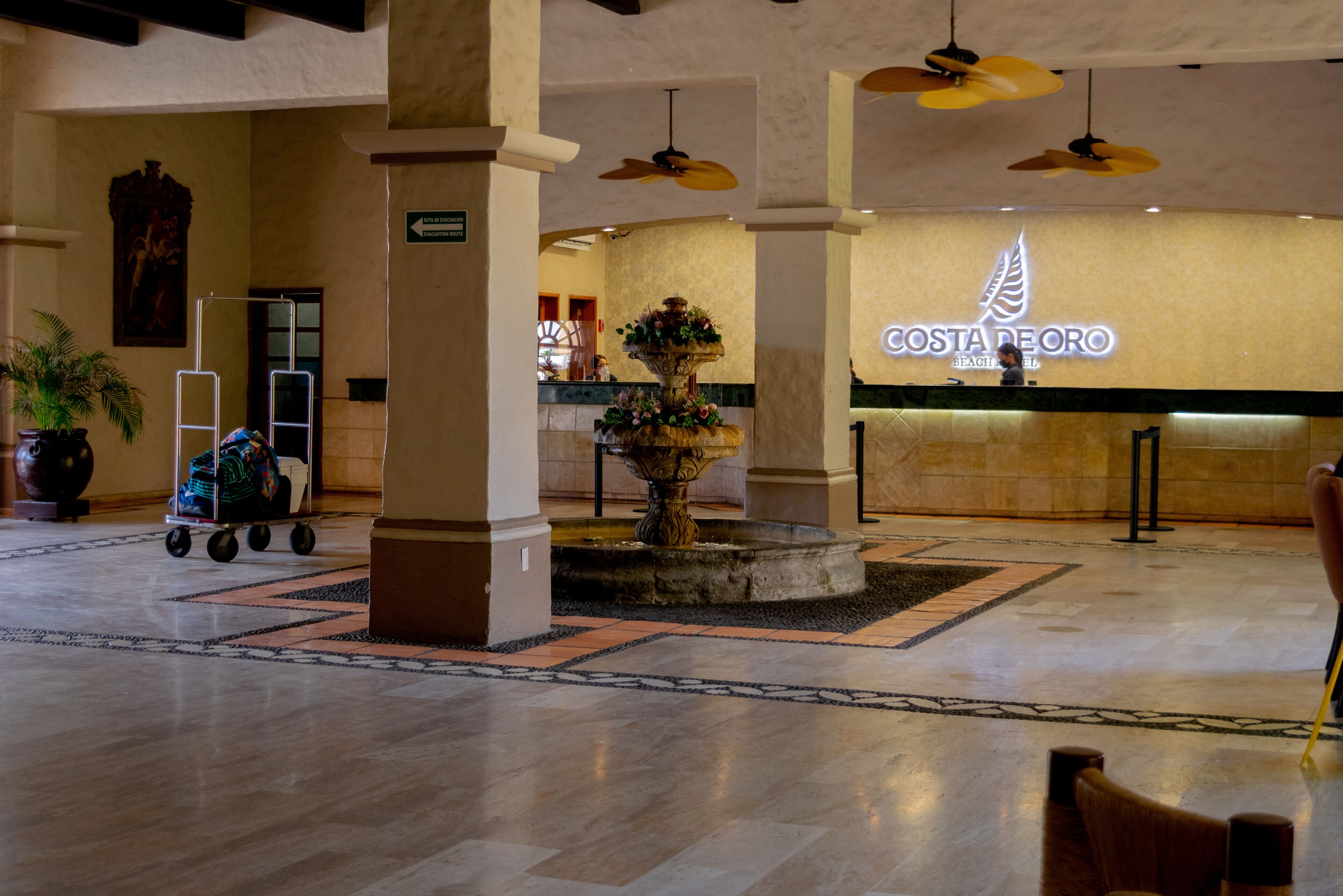A lobby with a reception desk, a fountain, and a luggage cart.
