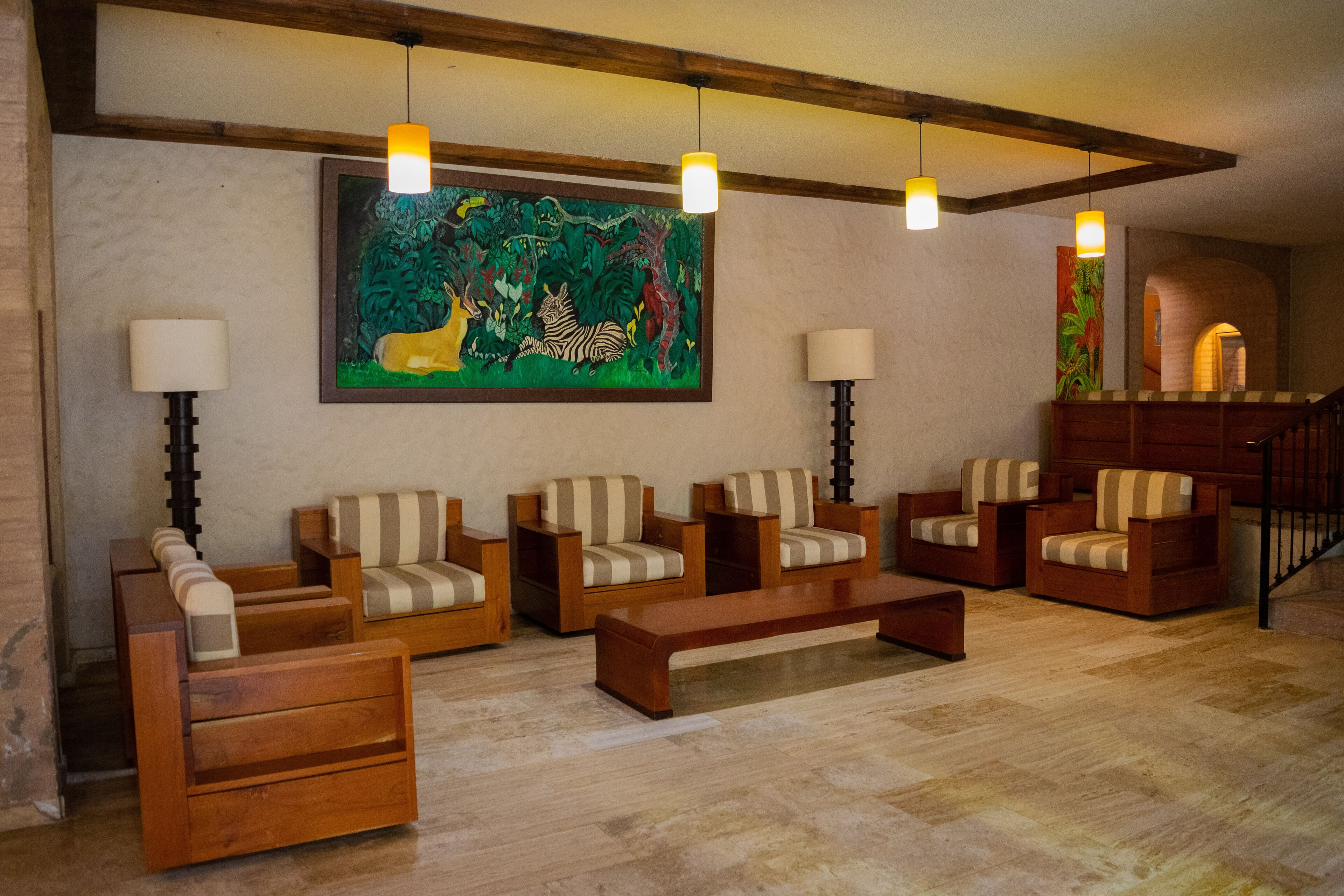 A spacious living room with wooden furniture, a large painting, and a staircase.