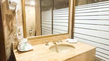 A bathroom with a beige sink, a large mirror, and a towel rack.