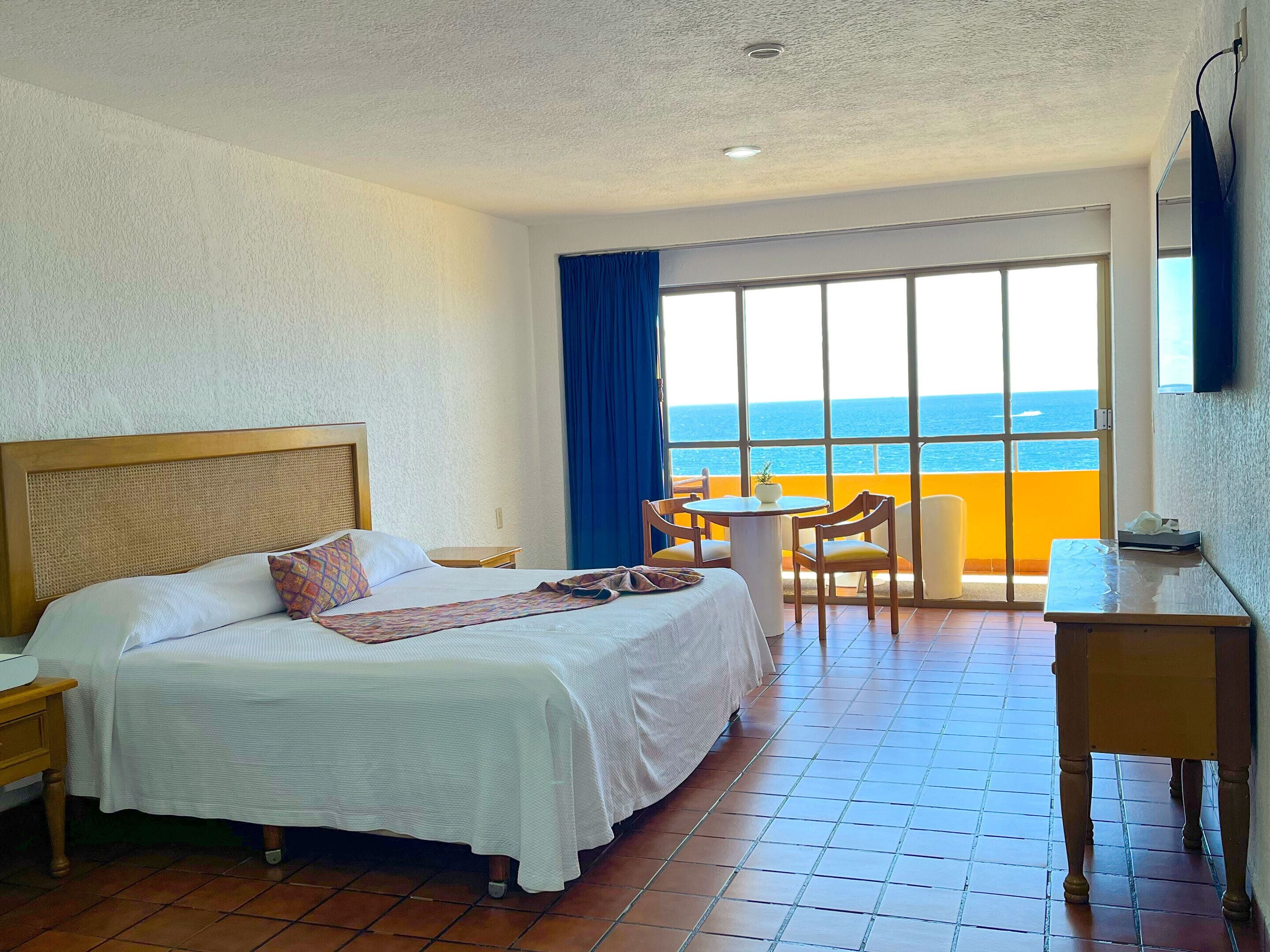 A hotel room with a large bed, a desk, and a view of the ocean.