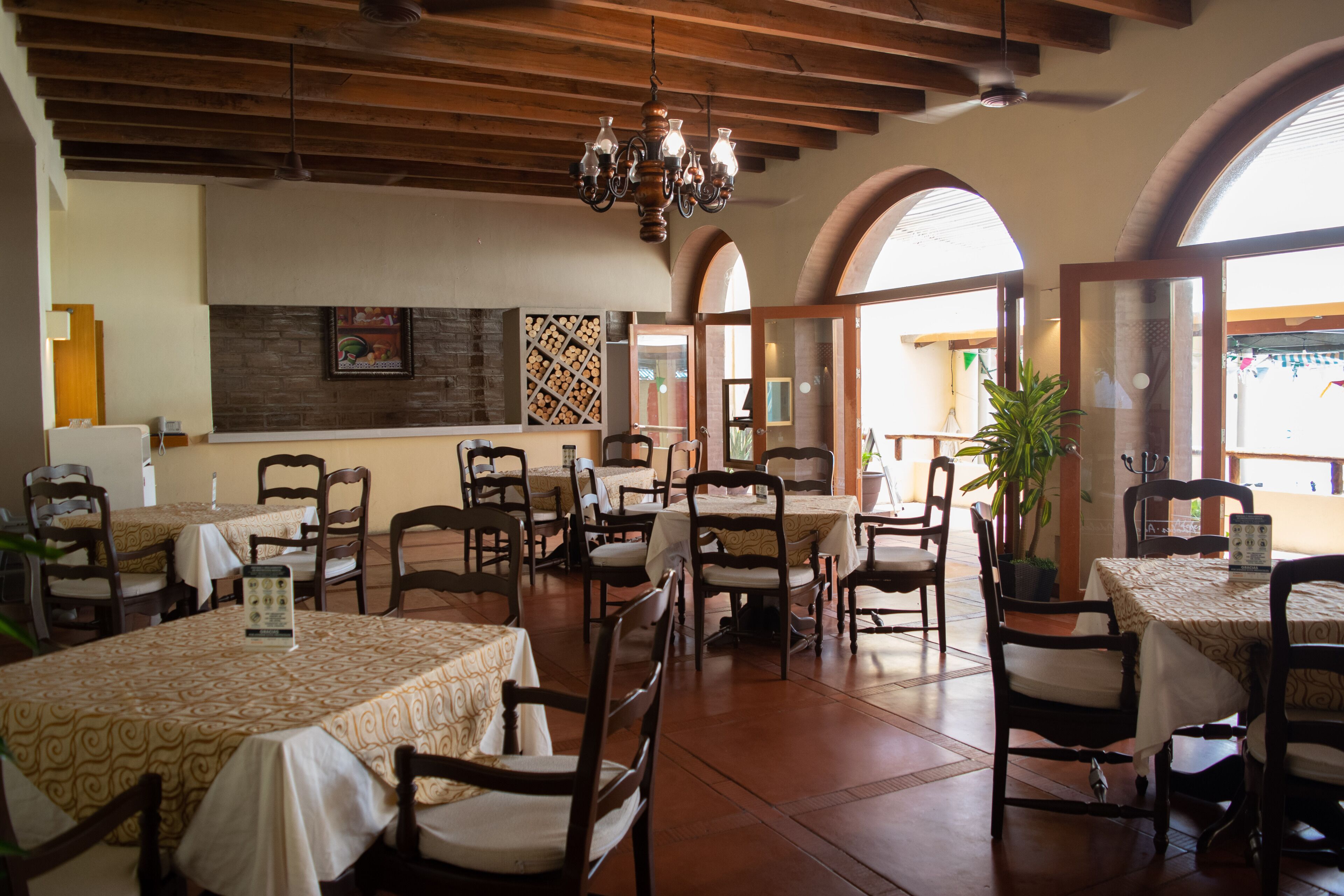Un ristorante con diversi tavoli e sedie, travi in legno a soffitto e ampie finestre.