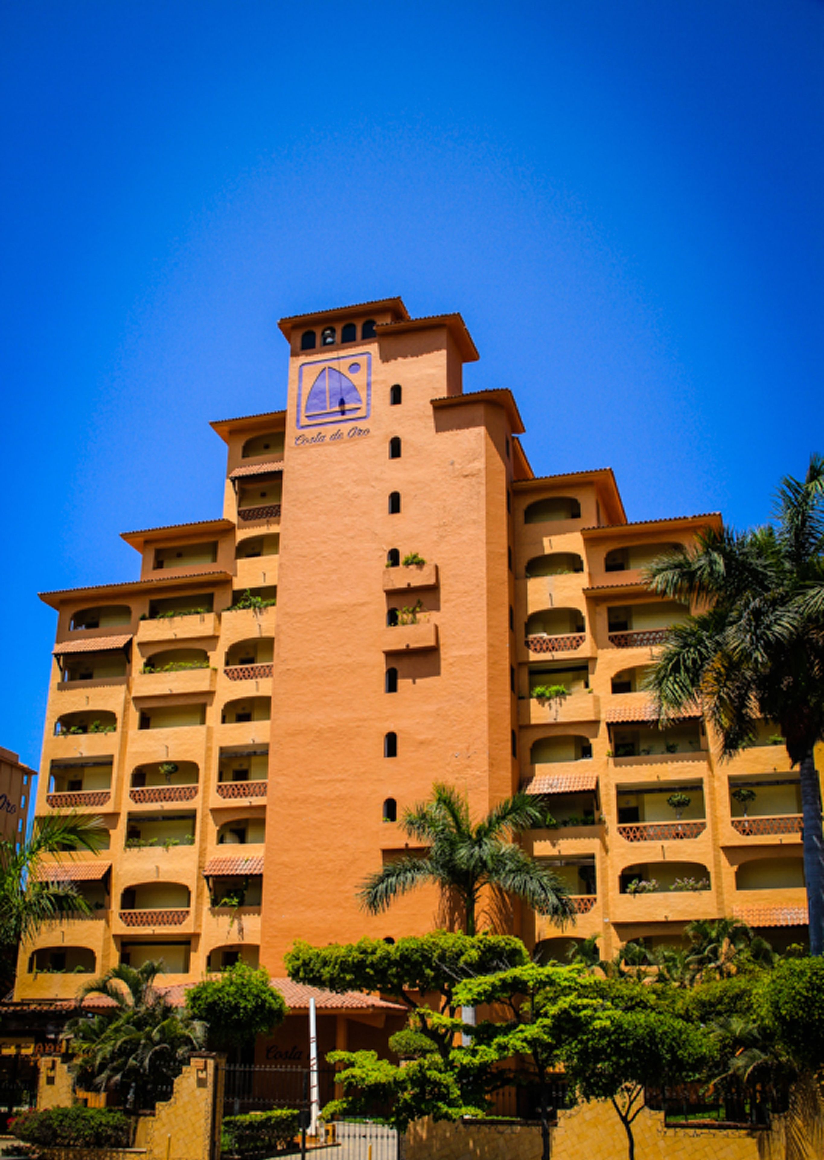 A multi-story hotel with a central tower, balconies, and lush greenery.