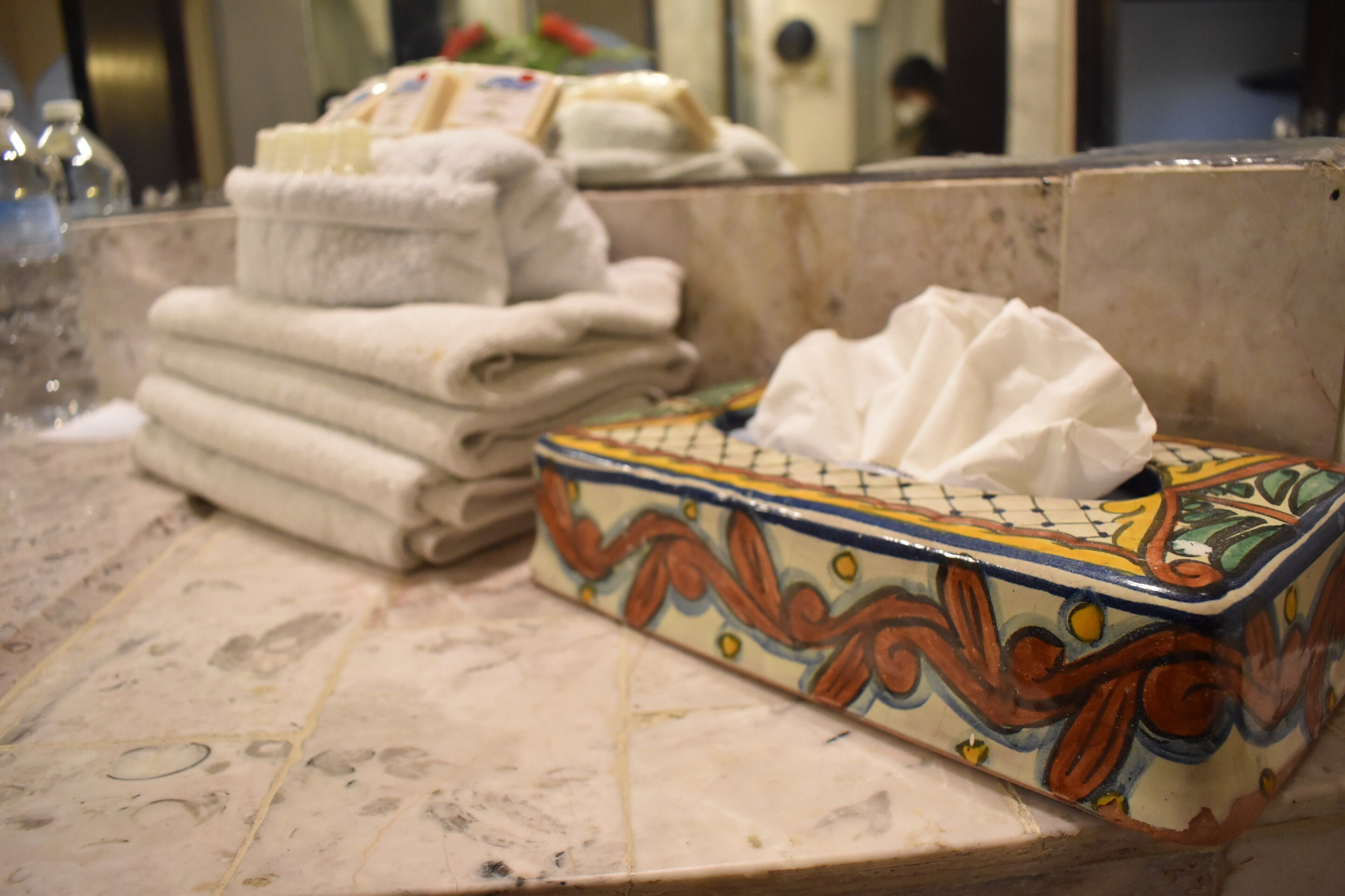 Un baño con encimera de mármol, una pila de toallas dobladas y una caja decorativa para pañuelos.