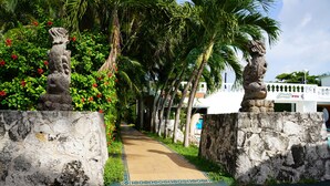 A pathway flanked by stone statues and palm trees, leading to a building with a sign that reads "B&B PUB." - Villablanca Garden Beach Hotel (Cozumel)